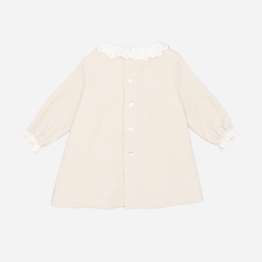 Sold at Bombon shop, designed by Fina Ejerique, a beige corduroy baby dress with smocked bodice, white ruffle collar, and long sleeves. back