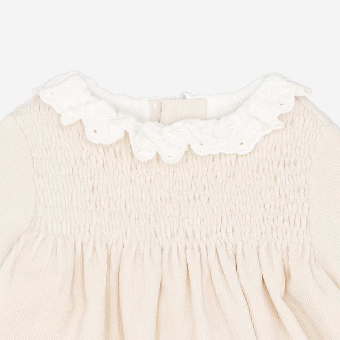 Sold at Bombon shop, designed by Fina Ejerique, a beige corduroy baby dress with smocked bodice, white ruffle collar, and long sleeves. zoom