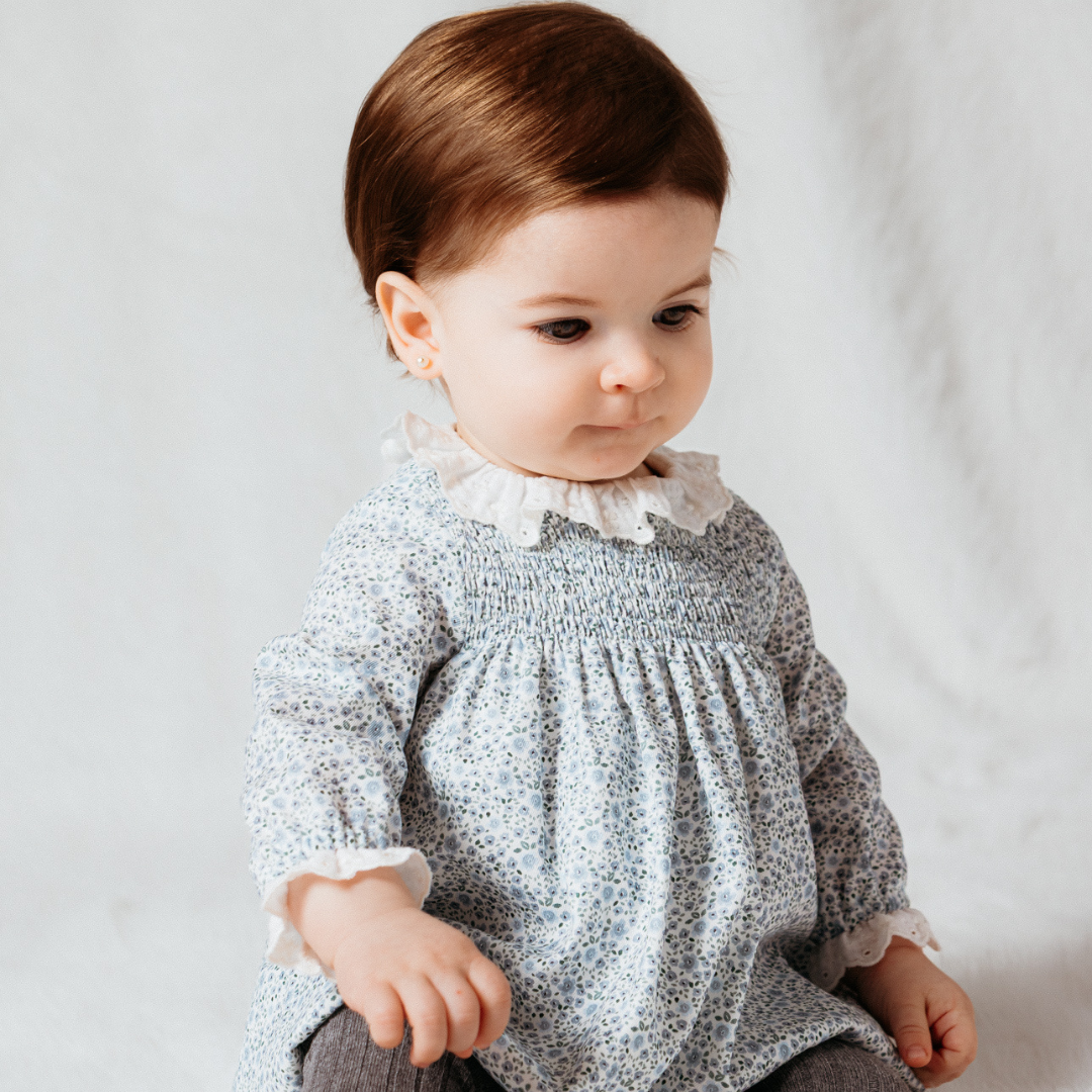 Sold at Bombon shop, designed by Fina Ejerique, a white floral viyella baby dress with smocked bodice, ruffle collar, and long sleeves. model