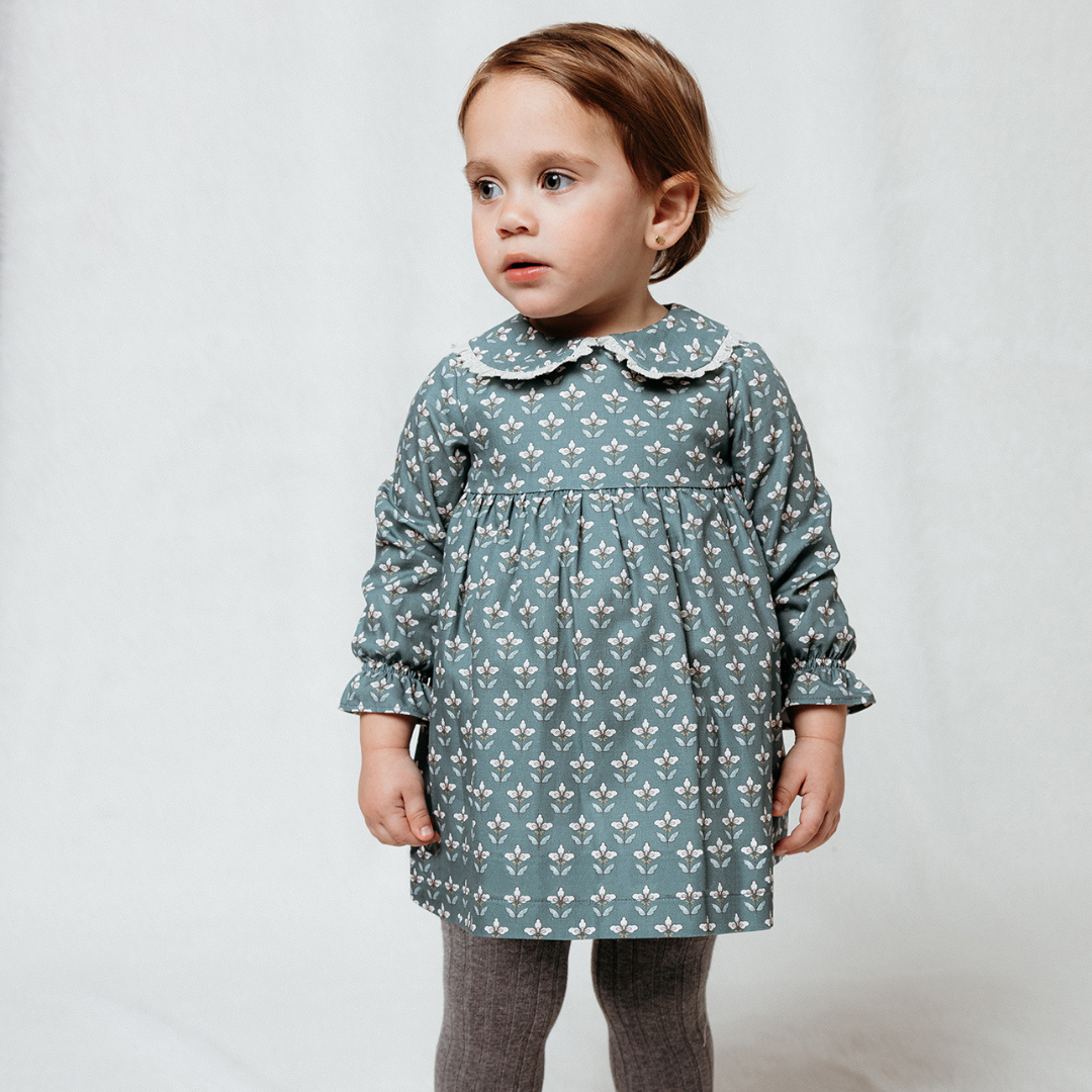 Sold at Bombon shop, designed by Fina Ejerique, a sage green floral baby dress with lace-trim collar and long sleeves. model