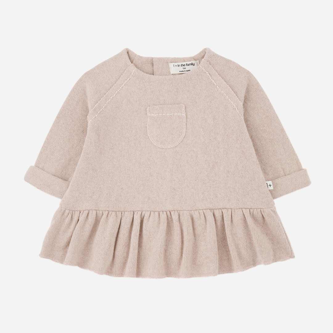 Sold at Bombon shop, designed by 1+ in the family — nude long-sleeve baby dress with ruffled hem and front patch pocket.