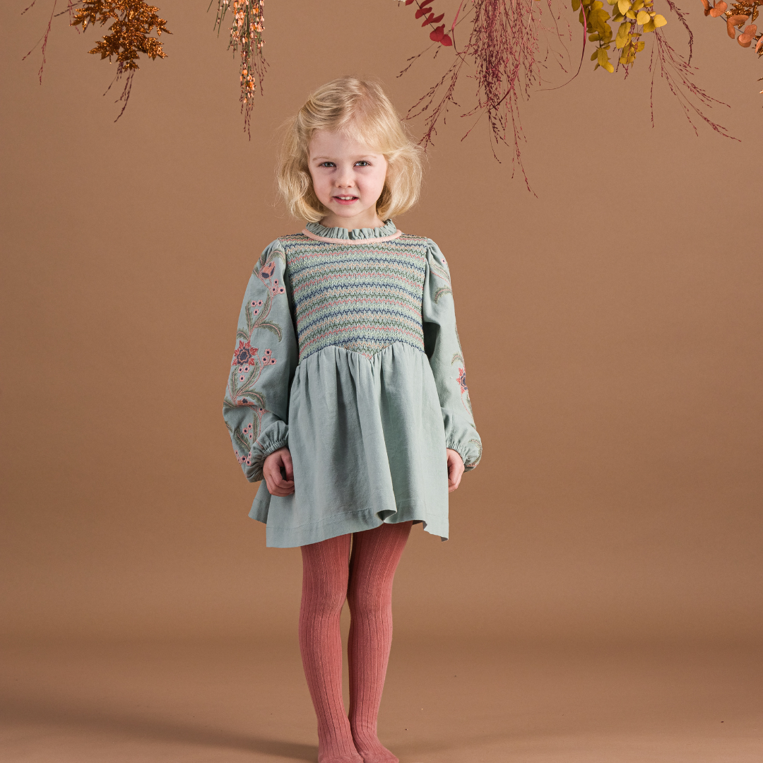 sold at Bombon shop, designed by Bachaa, Blouse/Short dress, Blue color, Organic cotton twill (167 g/m²), Plain lining in organic cotton voile, Long embroidered and elasticated sleeves, Smocked chest, Ruffled collar, Tone-on-tone buttons and belt at the back. Model view