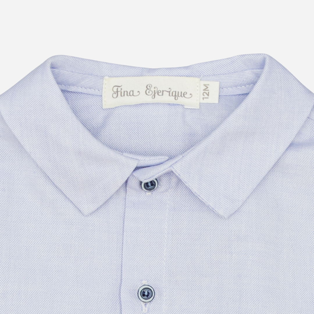 Sold at Bombon shop, designed by Fina Ejerique, a light-blue cotton baby shirt with rounded collar, long sleeves, and matching buttons. zoom