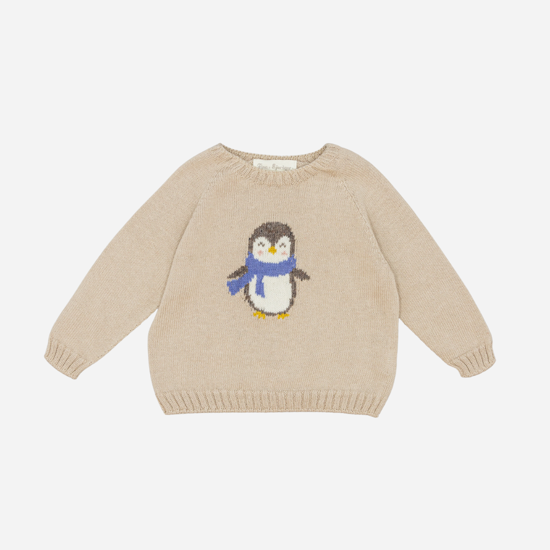 Sold at Bombon shop, designed by Fina Ejerique, a beige knit baby sweater with a penguin motif wearing a blue scarf. front