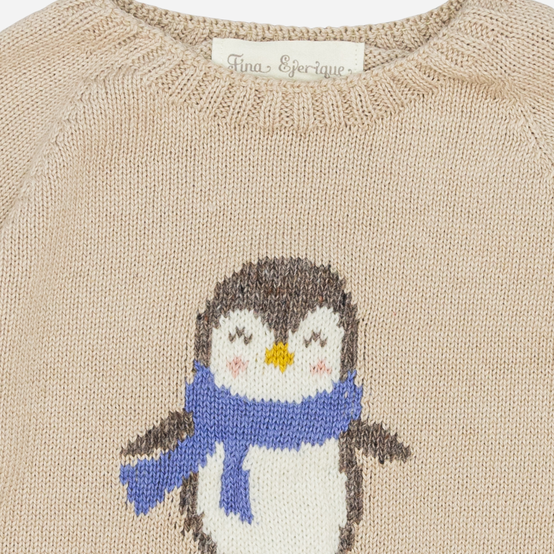 Sold at Bombon shop, designed by Fina Ejerique, a beige knit baby sweater with a penguin motif wearing a blue scarf. zoom