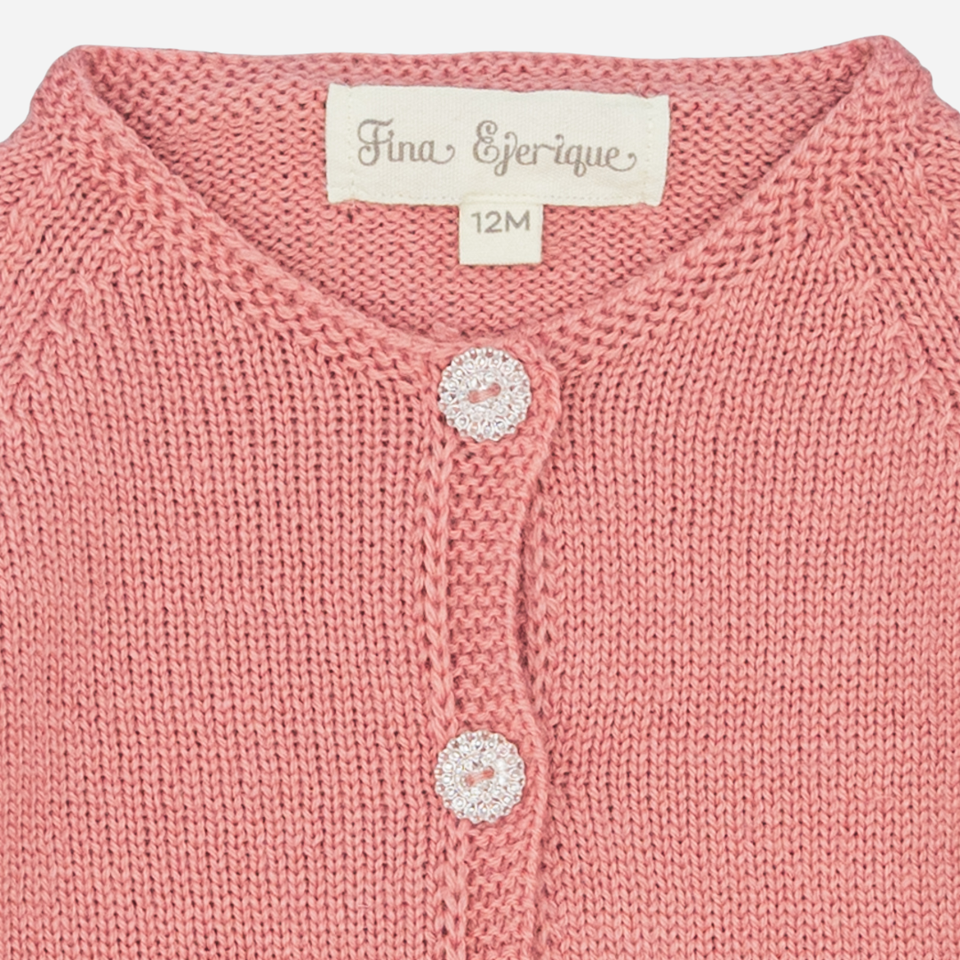 Sold at Bombon shop, designed by Fina Ejerique, a rose-pink knit baby cardigan with scalloped trim and front buttons. zoom