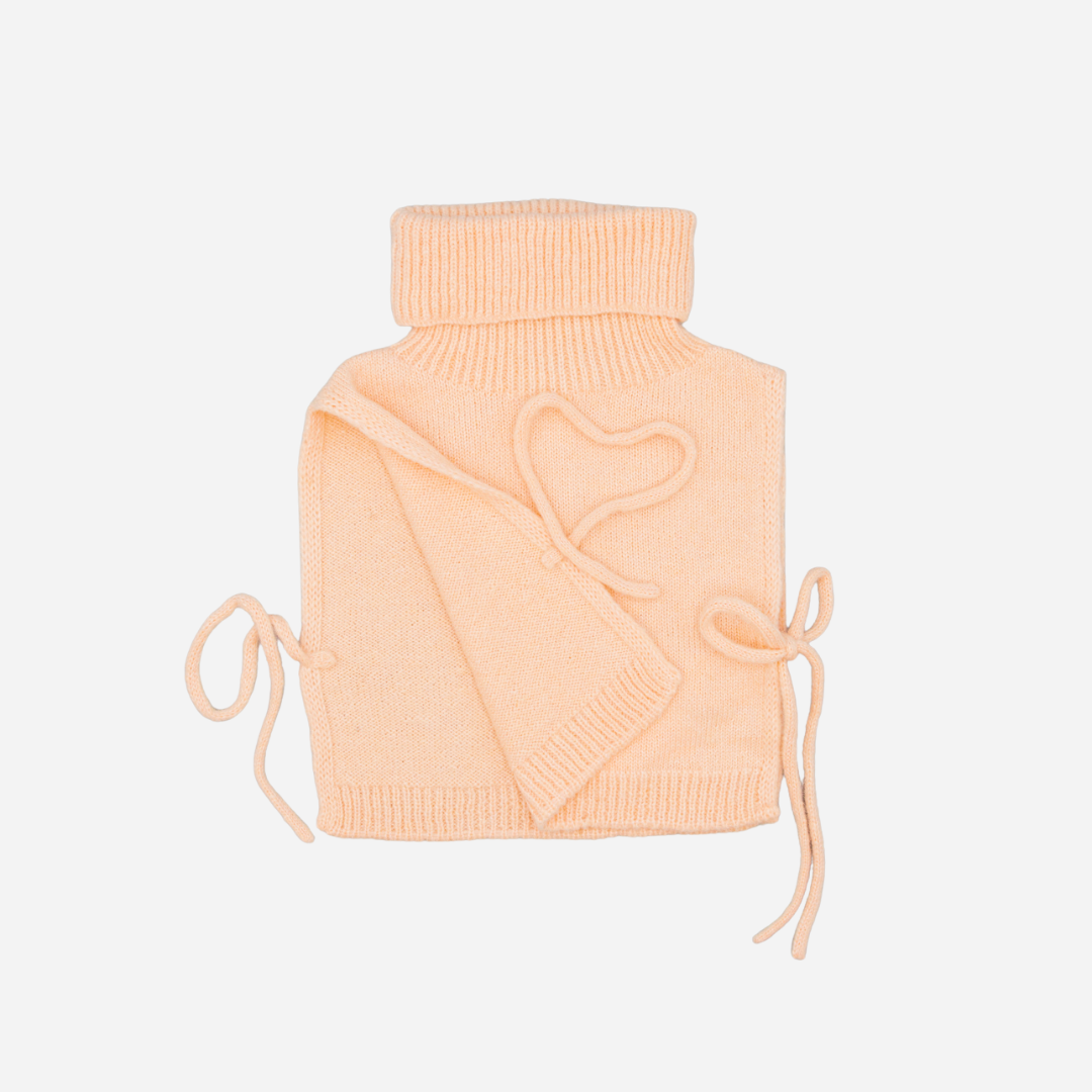 Sold at Bombon shop, designed by Fina Ejerique, pink knit vest with turtleneck and side ties, pairs perfectly with the floral blouse and beige textured skirt. side