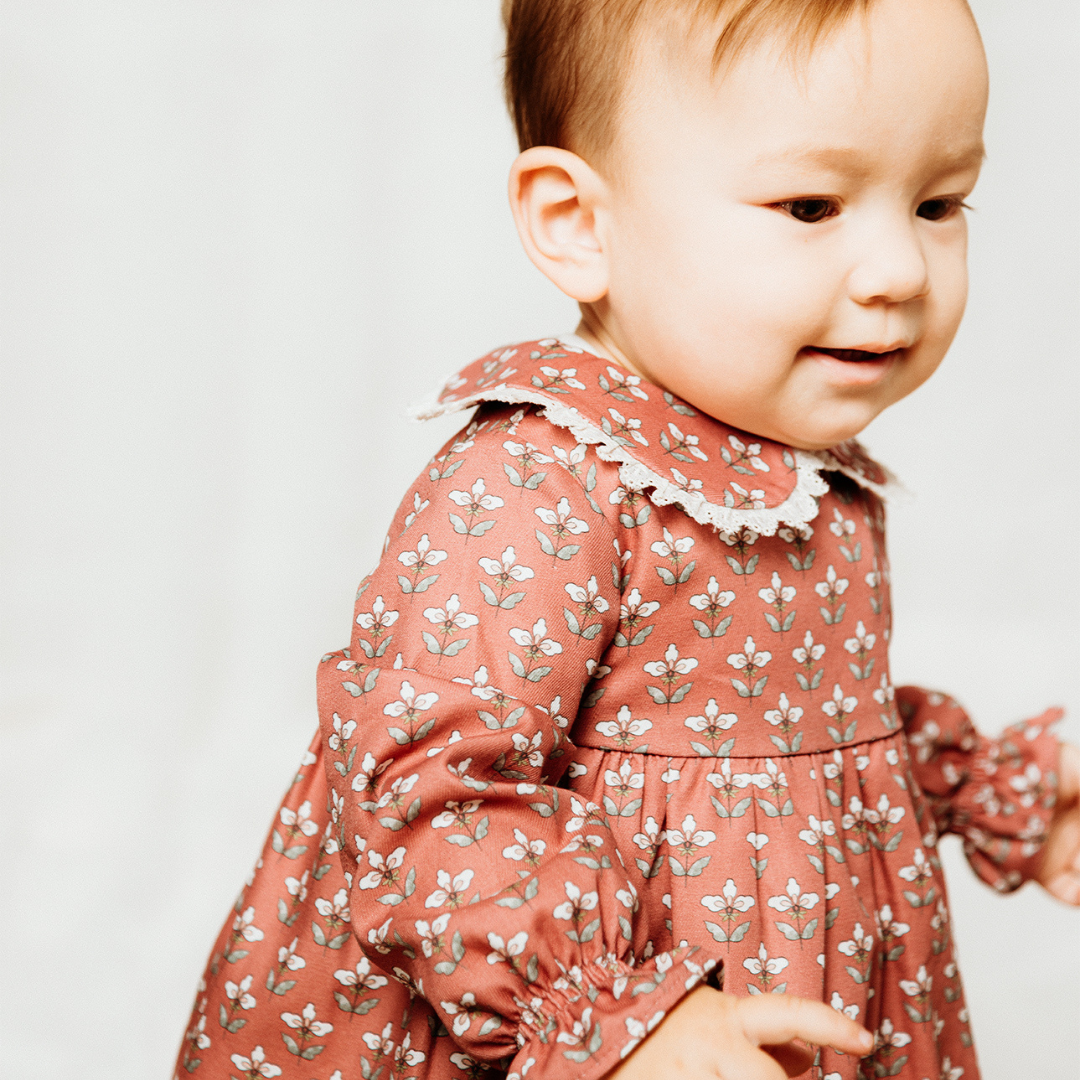Sold at Bombon shop, designed by Fina Ejerique, a coral-pink floral baby dress with lace-trim collar and long sleeves. model