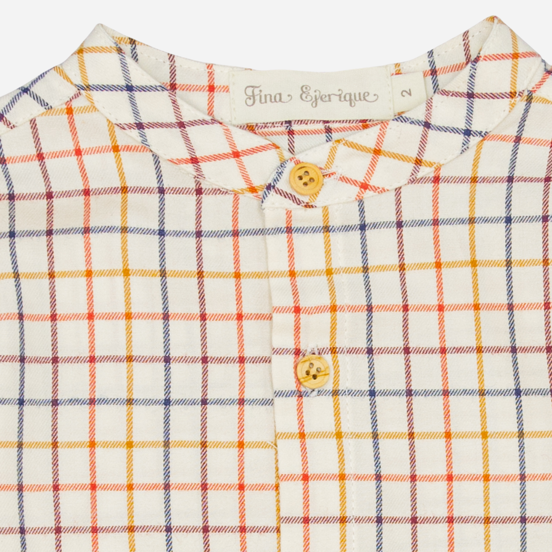 Sold at Bombon shop, designed by Fina Ejerique, a beige viyella baby shirt with red, mustard, and blue checkered pattern, wooden buttons, and long sleeves. zoom
