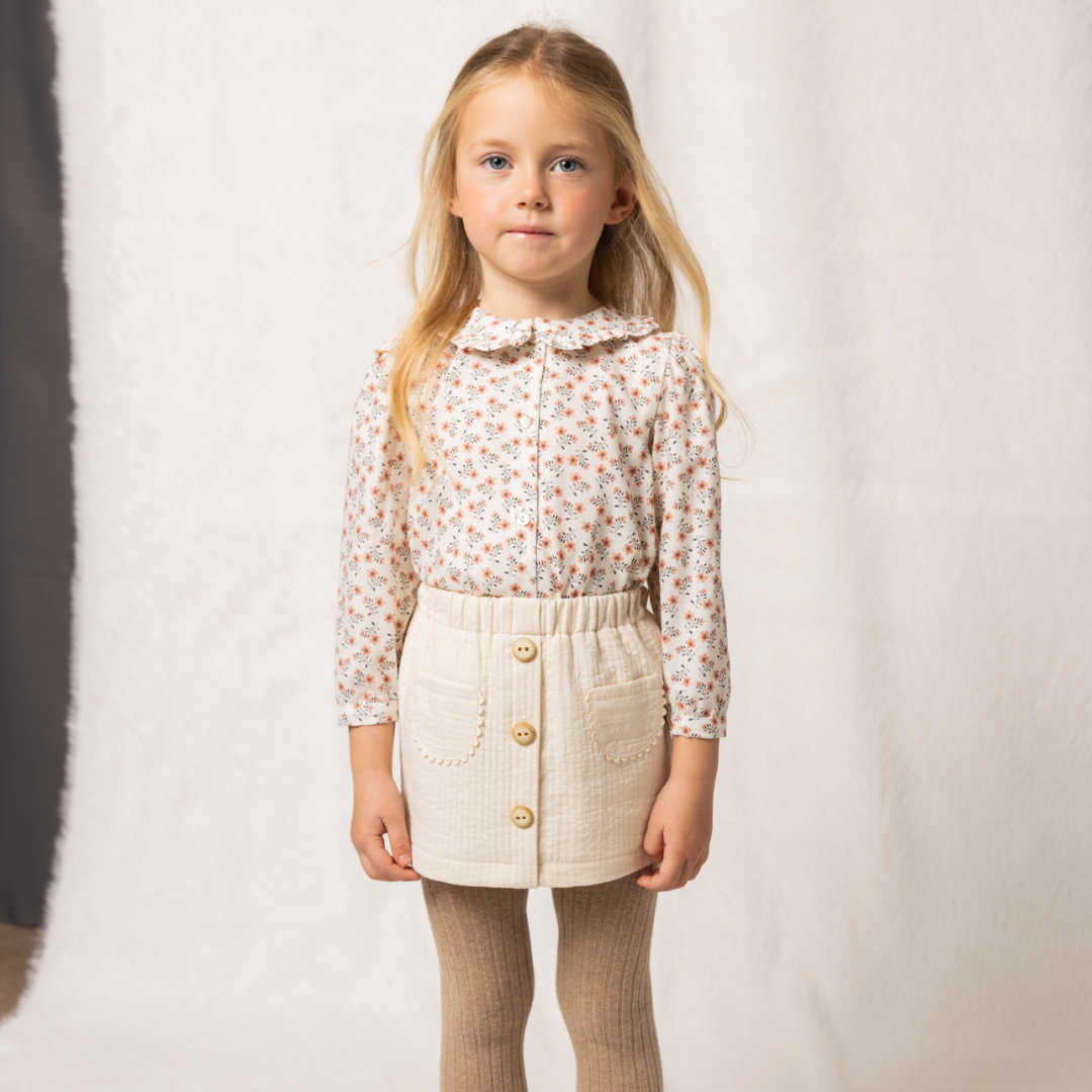 Sold at Bombon shop, designed by Fina Ejerique, beige textured skirt with button front and scalloped pockets, pairs perfectly with the floral blouse and pink vest. model