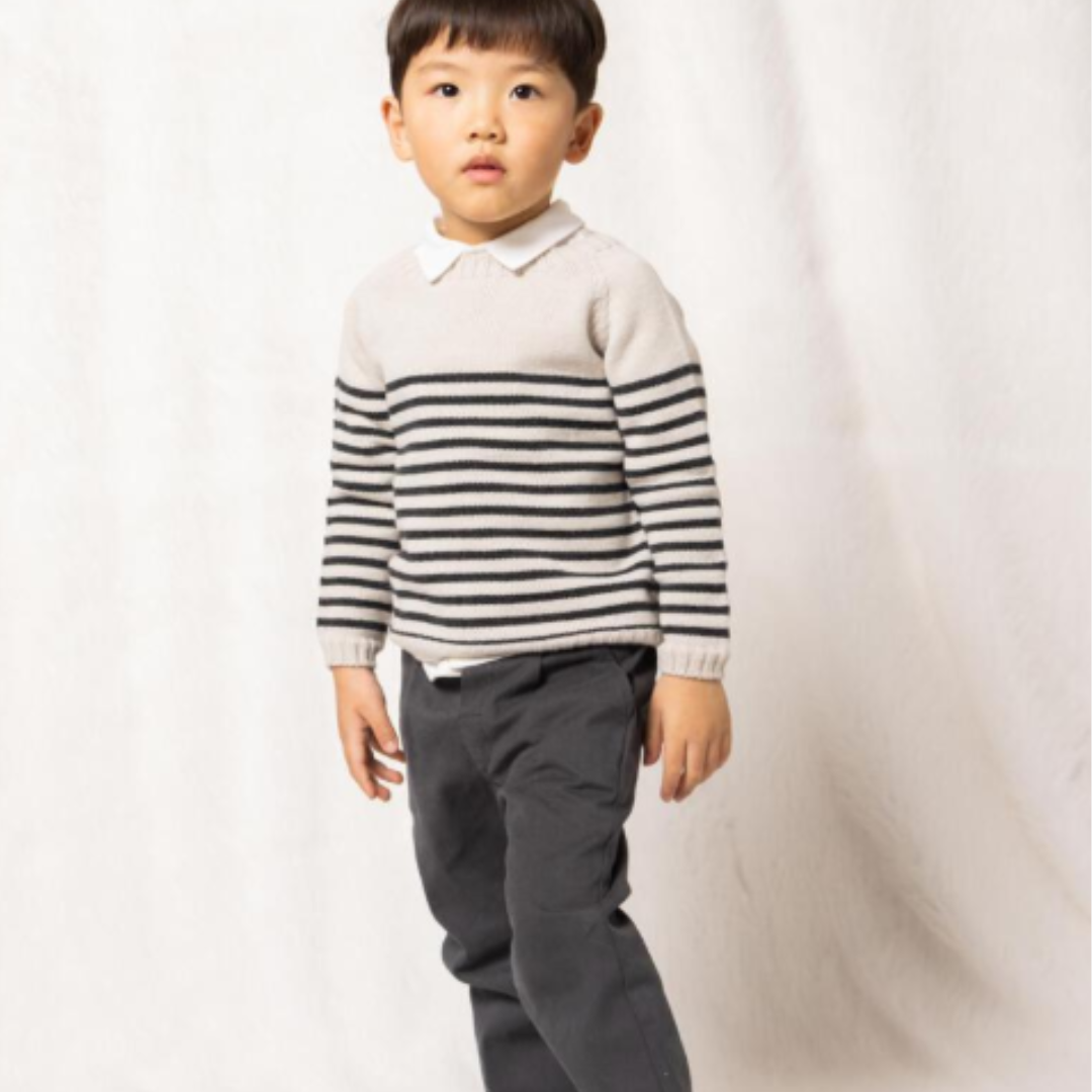 Sold at Bombon shop, designed by Fina Ejerique, a cream knit baby sweater with gray horizontal stripes, styled to pair with grey twill trousers. model
