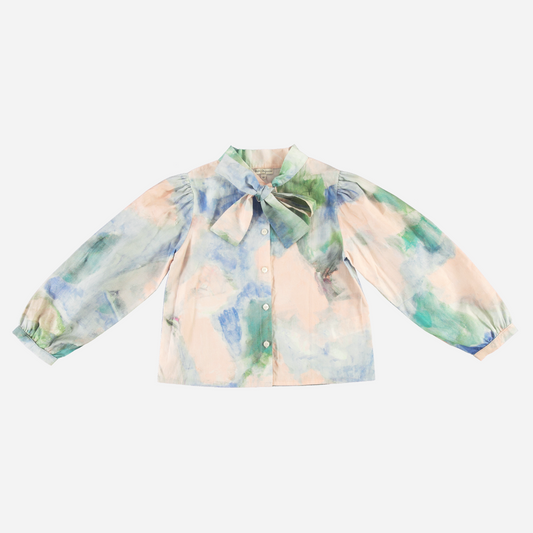 Sold at Bombon Shop, this Bebe Organic girls’ blouse features a watercolor-inspired print in soft pastel tones of blue, green, and peach, made from lightweight organic cotton with a statement bow collar and puffed long sleeves — a refined and artistic top perfect for special occasions or elevated everyday wear.