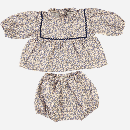 Sold at Bombon Shop, this Bebe Organic baby girl set features a delicate floral print in soft hues, with a ruffled collar, navy scalloped trim, and gathered long sleeves — paired with matching bloomers for a romantic, vintage-inspired look perfect for fall and winter wardrobes.