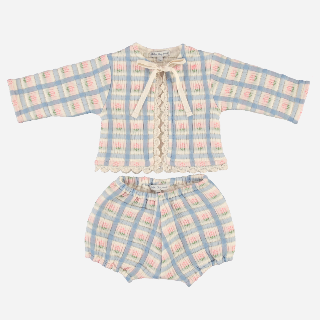Sold at Bombon Shop, this Bebe Organic baby girl outfit features a charming pastel plaid pattern in soft blue, pink, and cream tones, with a long-sleeve top adorned with lace trim, scalloped edges, and a delicate front tie, paired with matching bloomers — a vintage-inspired set made from organic cotton for comfort and timeless style.