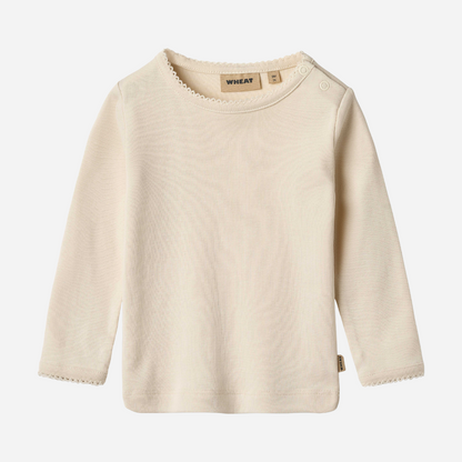 Sold at Bombon shop, designed by Wheat, this eggshell-colored ribbed long-sleeve tee features picot edging and a snap closure at the shoulder. front