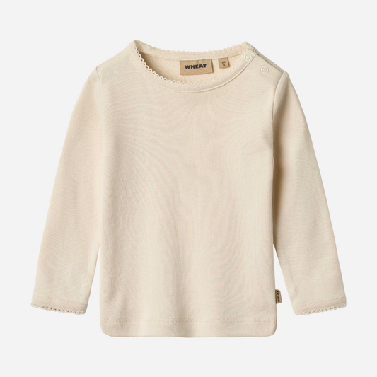Sold at Bombon shop, designed by Wheat, this eggshell-colored ribbed long-sleeve tee features picot edging and a snap closure at the shoulder. front