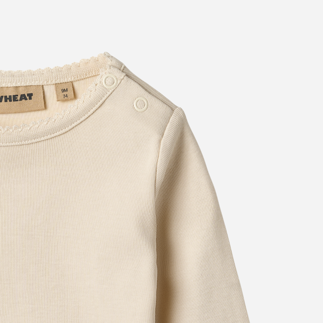 Sold at Bombon shop, designed by Wheat, this eggshell-colored ribbed long-sleeve tee features picot edging and a snap closure at the shoulder. top