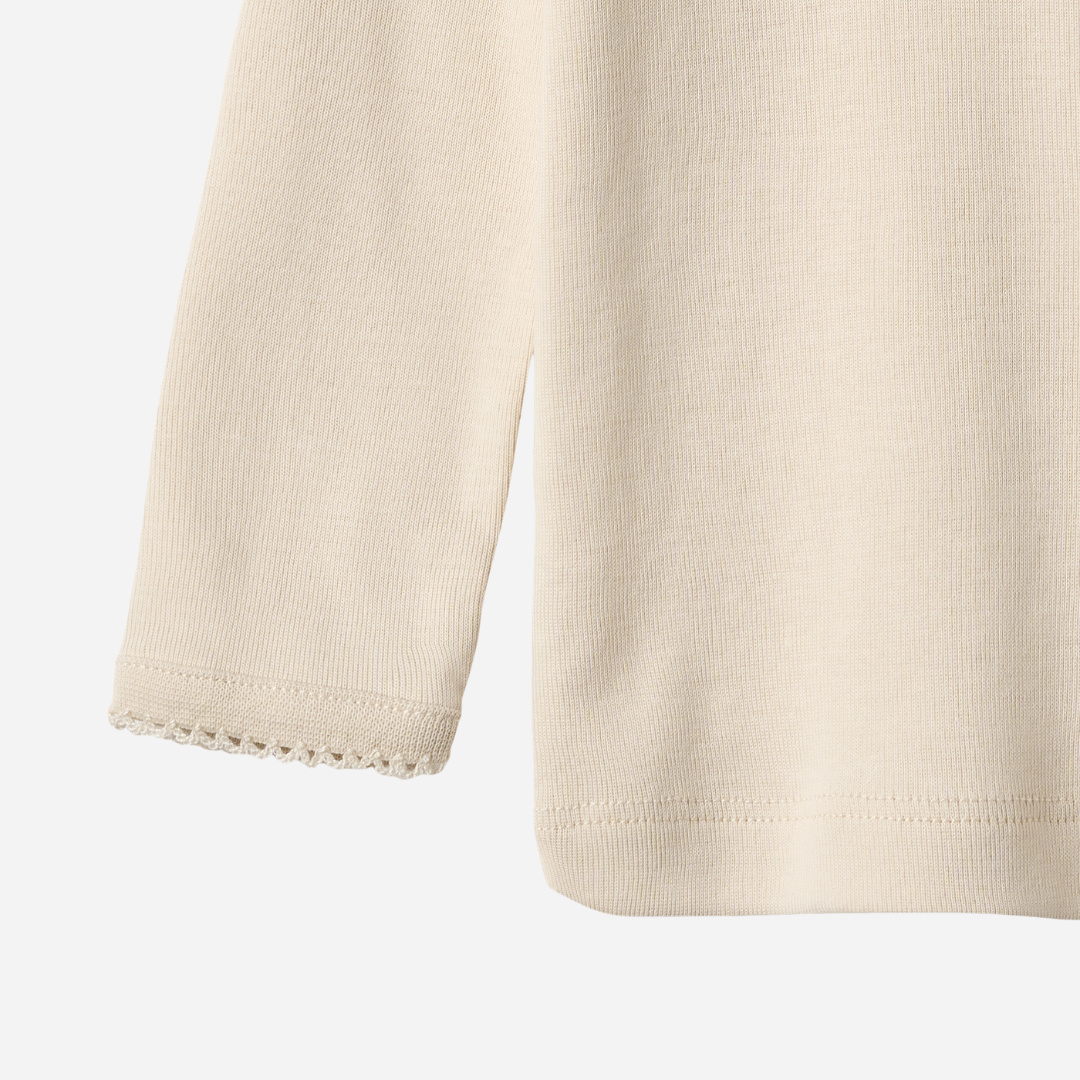 Sold at Bombon shop, designed by Wheat, this eggshell-colored ribbed long-sleeve tee features picot edging and a snap closure at the shoulder. bottom