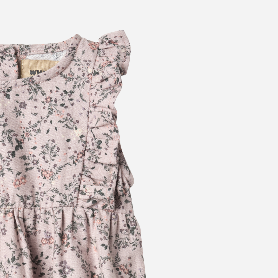 Sold at Bombon shop, designed by Wheat — sleeveless lilac floral baby romper with ruffled shoulders, gathered waist, and elasticized leg openings with snap closures for easy changing. top