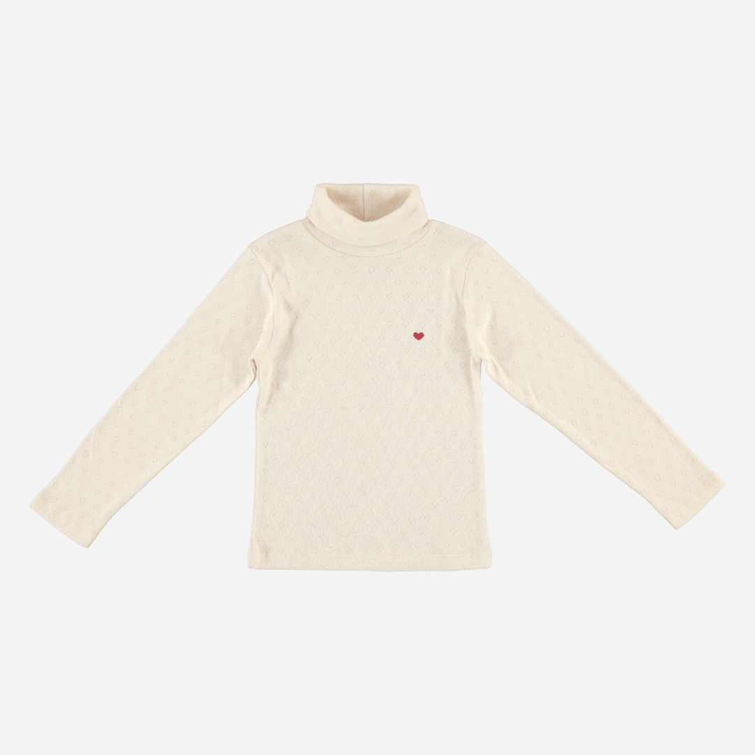 Sold at Bombon Shop, this Bebe Organic girls’ turtleneck top is crafted from soft organic cotton in an ivory pointelle knit, featuring long sleeves, a high neckline for warmth, and a subtle embroidered red heart — a cozy layering essential with a sweet, minimalist touch.