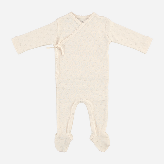 Sold at Bombon Shop, this Bebe Organic newborn footed romper is crafted from ultra-soft organic cotton in a delicate ivory pointelle knit, featuring a wrap-style front with side tie and snap closures for easy changing — a gentle and timeless essential for baby’s first wardrobe.