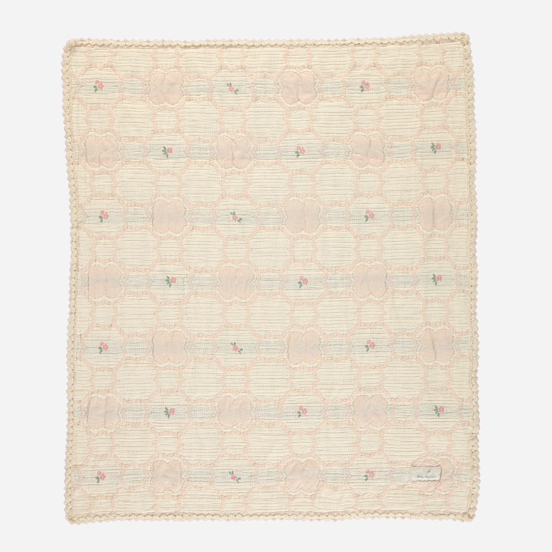 Sold at Bombon Shop, this Bebe Organic baby blanket is crafted from ultra-soft organic cotton in a vintage-inspired woven floral pattern with soft peach and green tones, finished with scalloped crochet trim — a delicate and cozy essential perfect for swaddling, stroller rides, or heirloom-quality nursery decor.