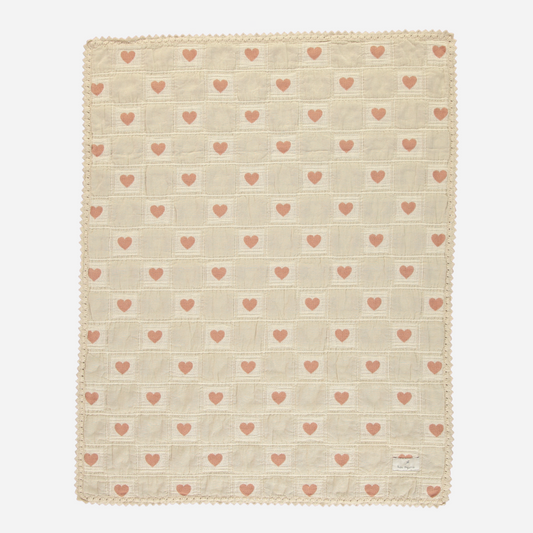 Sold at Bombon Shop, this Bebe Organic baby blanket is made from soft organic cotton muslin in a sweet ivory and blush pink heart pattern, featuring a textured checkered weave and delicate scalloped crochet trim — a cozy and adorable essential for swaddling, cuddling, or nursery decor.