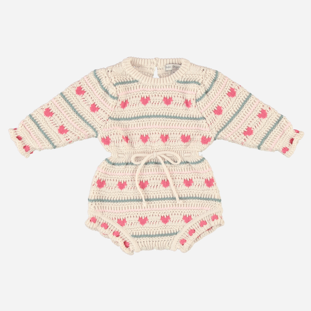 Sold at Bombon Shop, this Bebe Organic baby girl knit romper is made from soft organic cotton with an adorable pink heart and stripe pattern, featuring long sleeves, a cinched waist with drawstring tie, and ruffled leg openings — a cozy and playful piece perfect for cooler days and special moments.