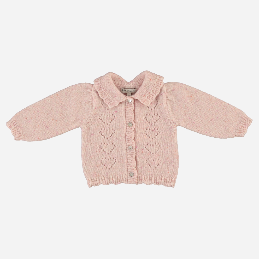 Sold at Bombon Shop, this Bebe Organic baby and toddler girl cardigan is crafted from soft pink wool with delicate heart-shaped knit details, ruffled collar, and front button closure — pair it with the matching knit pants for a cozy, coordinated look perfect for fall and winter layering.