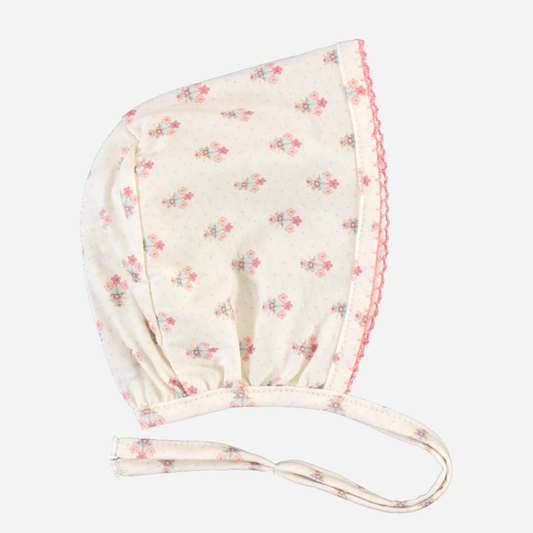 Sold at Bombon Shop, this Bebe Organic baby bonnet is made from soft organic cotton in a delicate floral print with pink scalloped trim and tie closure — pair with the matching footed romper for an adorable and cozy newborn outfit perfect for everyday wear or special gifting.