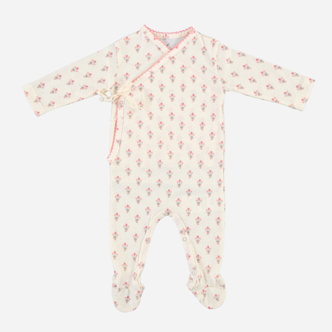 Sold at Bombon Shop, this Bebe Organic baby girl footed romper is made from soft organic cotton in a delicate floral print with pink trim, featuring a wrap-style front with bow tie closure for easy dressing — pair with the matching bonnet for a sweet and cozy newborn outfit perfect for everyday wear or gifting.