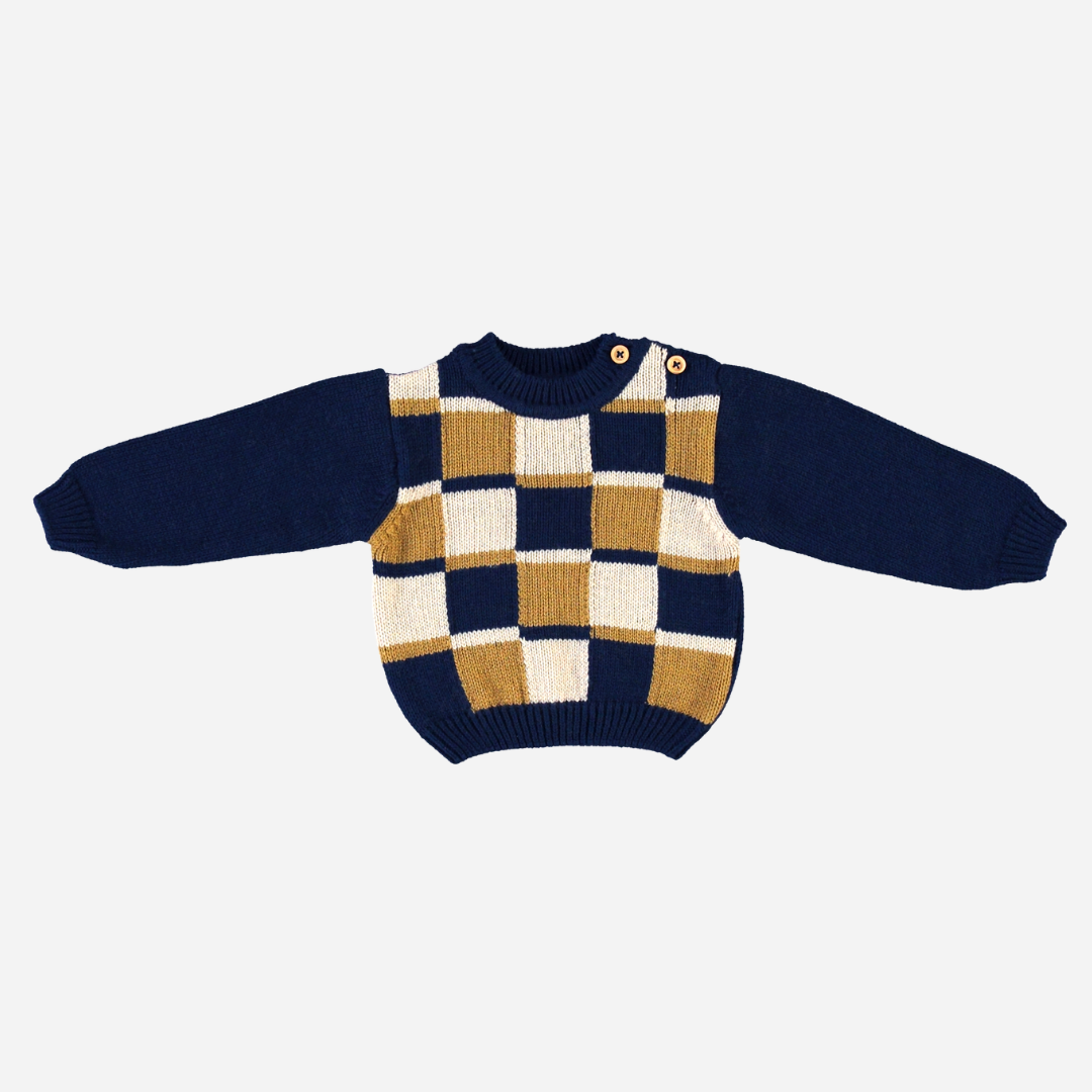 Sold at Bombon Shop, this Bebe Organic baby and toddler sweater is crafted from soft organic wool and features a bold checkered pattern in navy, mustard, and cream with button details at the shoulder — a cozy and stylish knit perfect for chilly fall and winter days.