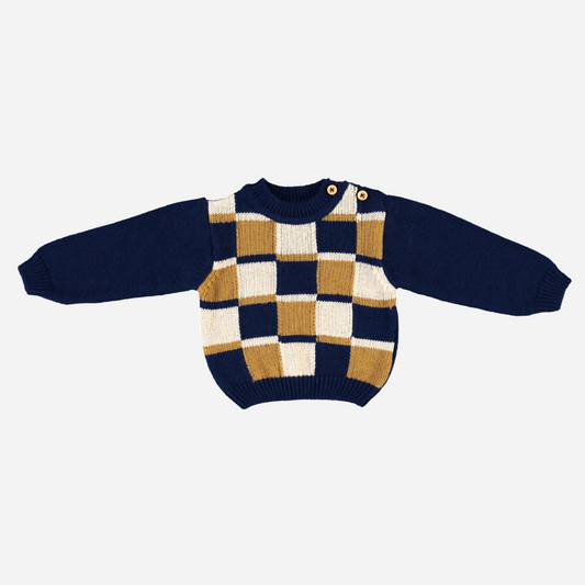 Sold at Bombon Shop, this Bebe Organic baby and toddler sweater is crafted from soft organic wool and features a bold checkered pattern in navy, mustard, and cream with button details at the shoulder — a cozy and stylish knit perfect for chilly fall and winter days.