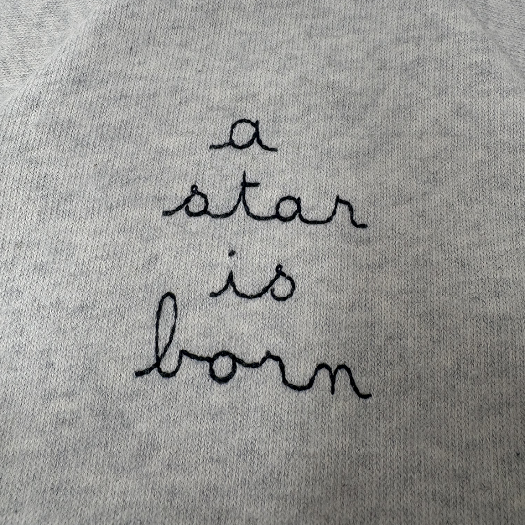 Sold at Bombon shop, designed by Tiny Soul — grey cotton baby romper with “a star is born” embroidery and bottom snap closures. detail