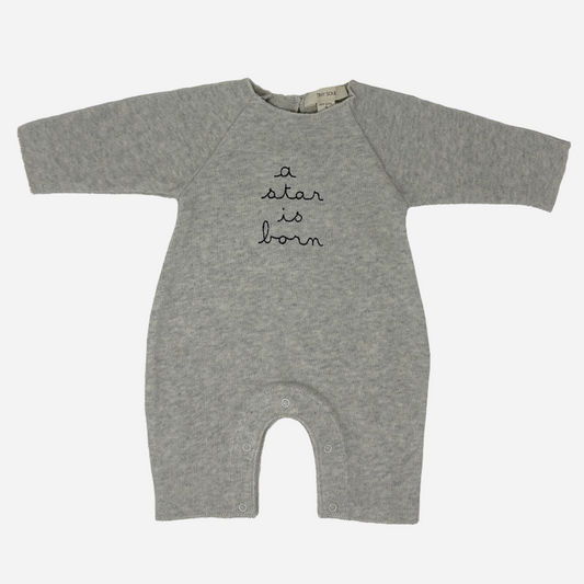 Sold at Bombon shop, designed by Tiny Soul — grey cotton baby romper with “a star is born” embroidery and bottom snap closures. front