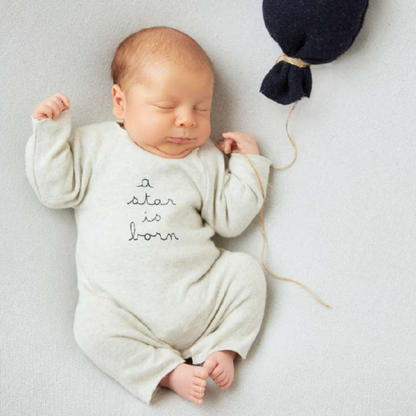 Sold at Bombon shop, designed by Tiny Soul — grey cotton baby romper with “a star is born” embroidery and bottom snap closures. model