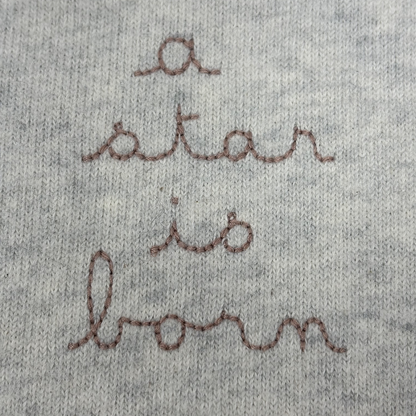 Sold at Bombon shop, designed by Tiny Soul — grey cotton baby romper with “a star is born” embroidery and bottom snap closures. detail