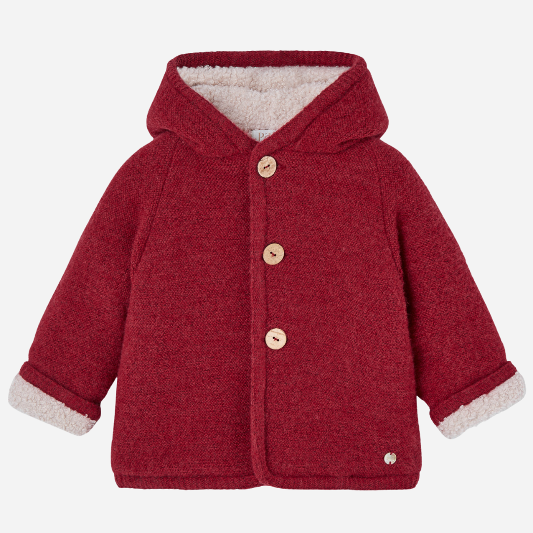 Sold at Bombon shop, designed by Paz Rodriguez, red hooded winter coat with faux-shearling lining and wooden buttons from the Acebo collection