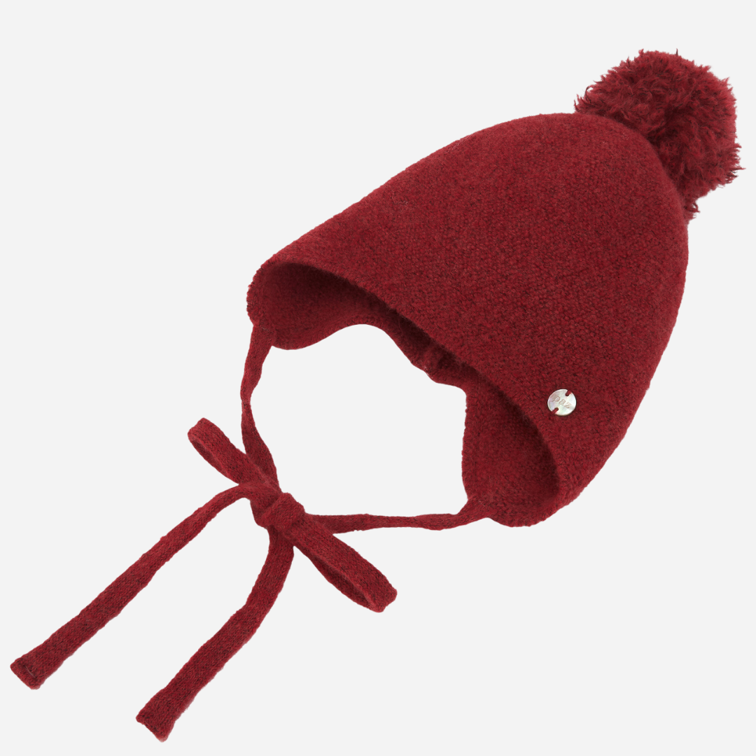 Sold at Bombon shop, designed by Paz Rodriguez, red wool baby bonnet with pom-pom and ties, part of the Acebo collection.