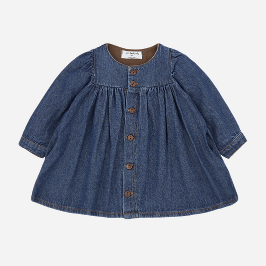 Sold at Bombon shop, designed by 1+ in the family — soft denim baby dress with long sleeves, wooden buttons, and gathered waist. front