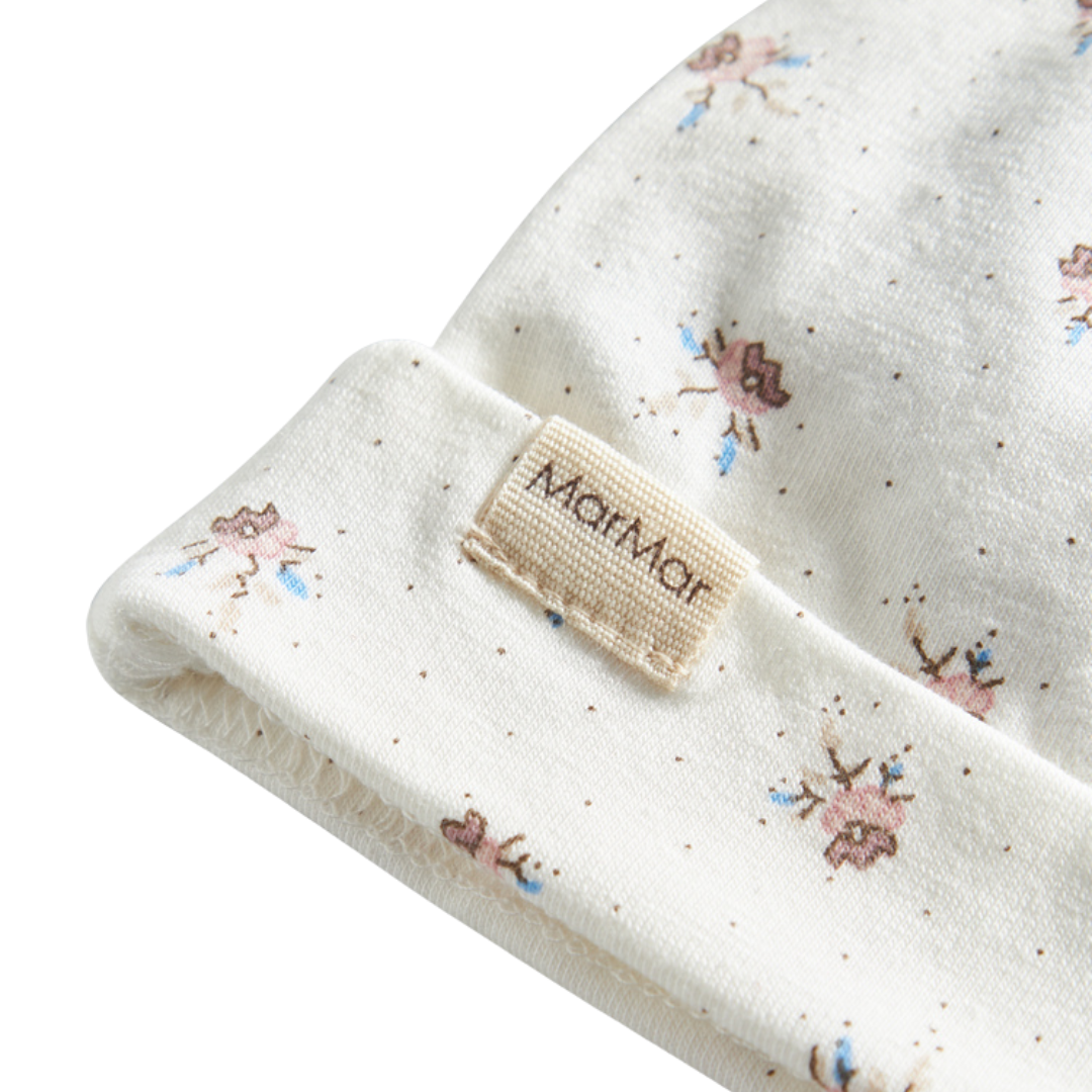 Sold at Bombon shop, designed by MarMar Copenhagen — white organic cotton baby hat with floral print and top knot, part of a matching set.