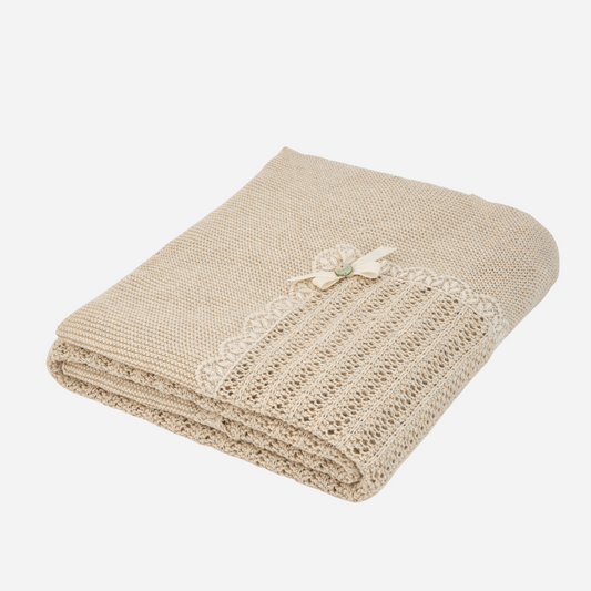 Sold at Bombon shop, designed by Paz Rodriguez: folded beige knit baby blanket with lace trim and pink bow detail.