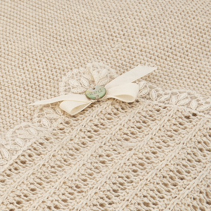 Sold at Bombon shop, designed by Paz Rodriguez: folded beige knit baby blanket with lace trim and pink bow detail.