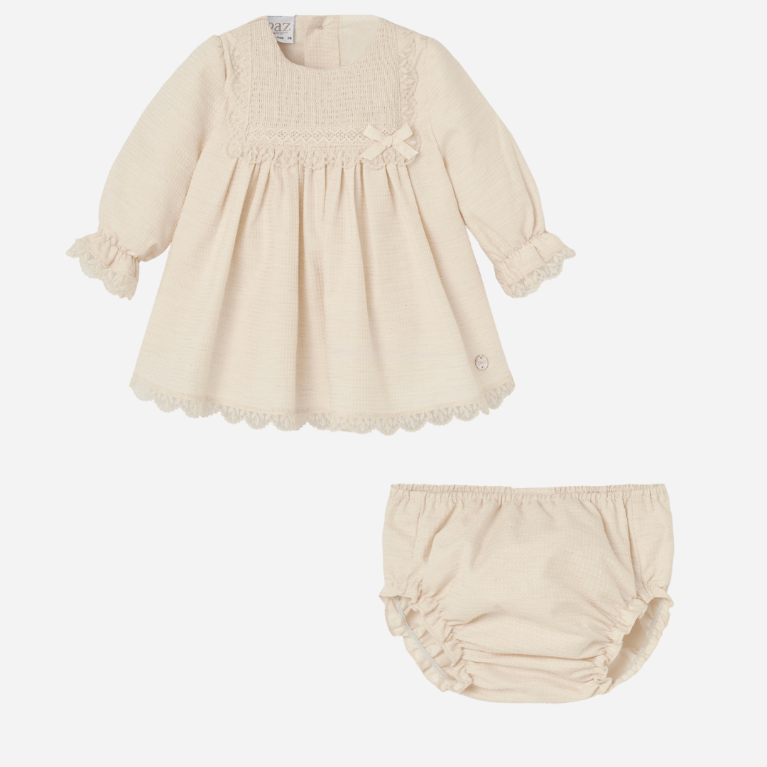Sold at Bombon shop, designed by Paz Rodriguez, beige baby dress with lace trim, smocked bodice, and matching bloomers.