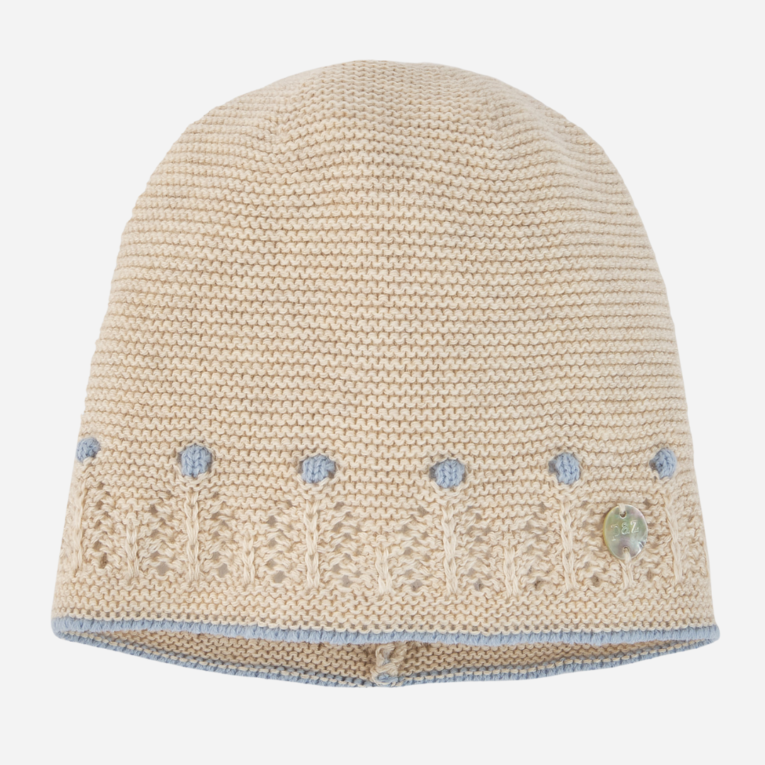 Sold at Bombon shop, designed by Paz Rodriguez. Beige knit baby hat with blue embroidered accents and delicate openwork trim, pairs with Alegría knit set.