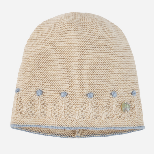 Sold at Bombon shop, designed by Paz Rodriguez. Beige knit baby hat with blue embroidered accents and delicate openwork trim, pairs with Alegría knit set.