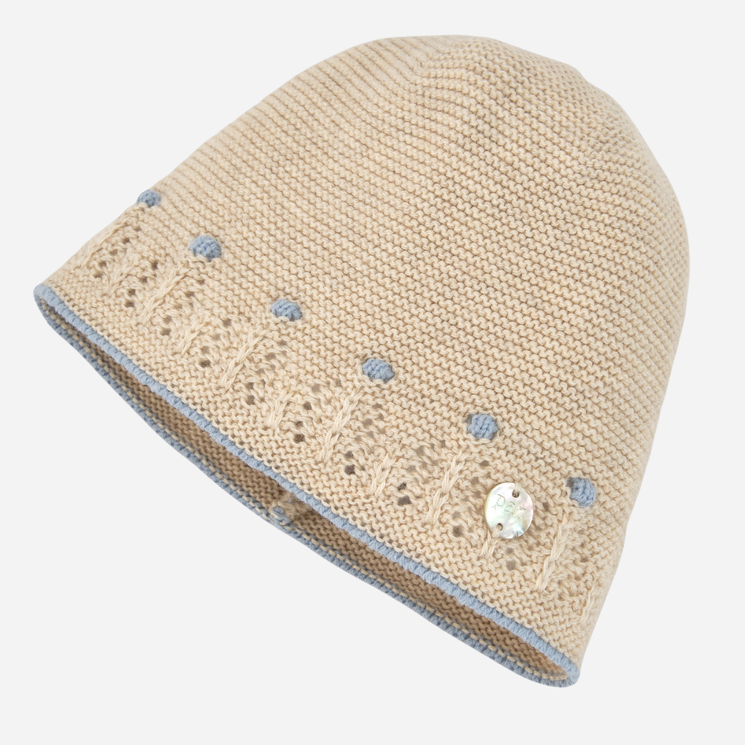 Sold at Bombon shop, designed by Paz Rodriguez. Beige knit baby hat with blue embroidered accents and delicate openwork trim, pairs with Alegría knit set.