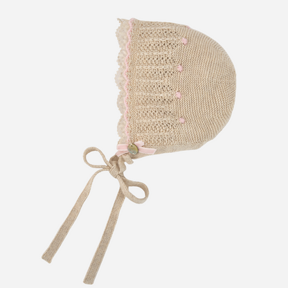Sold at Bombon shop, designed by Paz Rodriguez: beige knit baby bonnet with lace trim and pink accents.