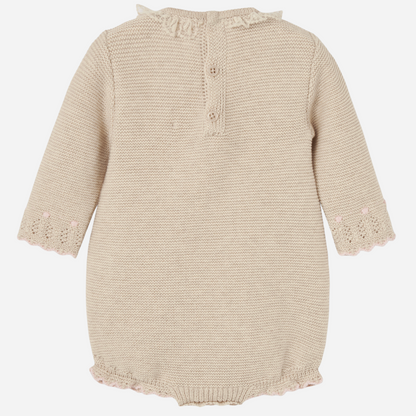 Sold at Bombon shop, designed by Paz Rodriguez, beige knit baby romper with lace detail, scalloped trim, and a pink bow on the waist.