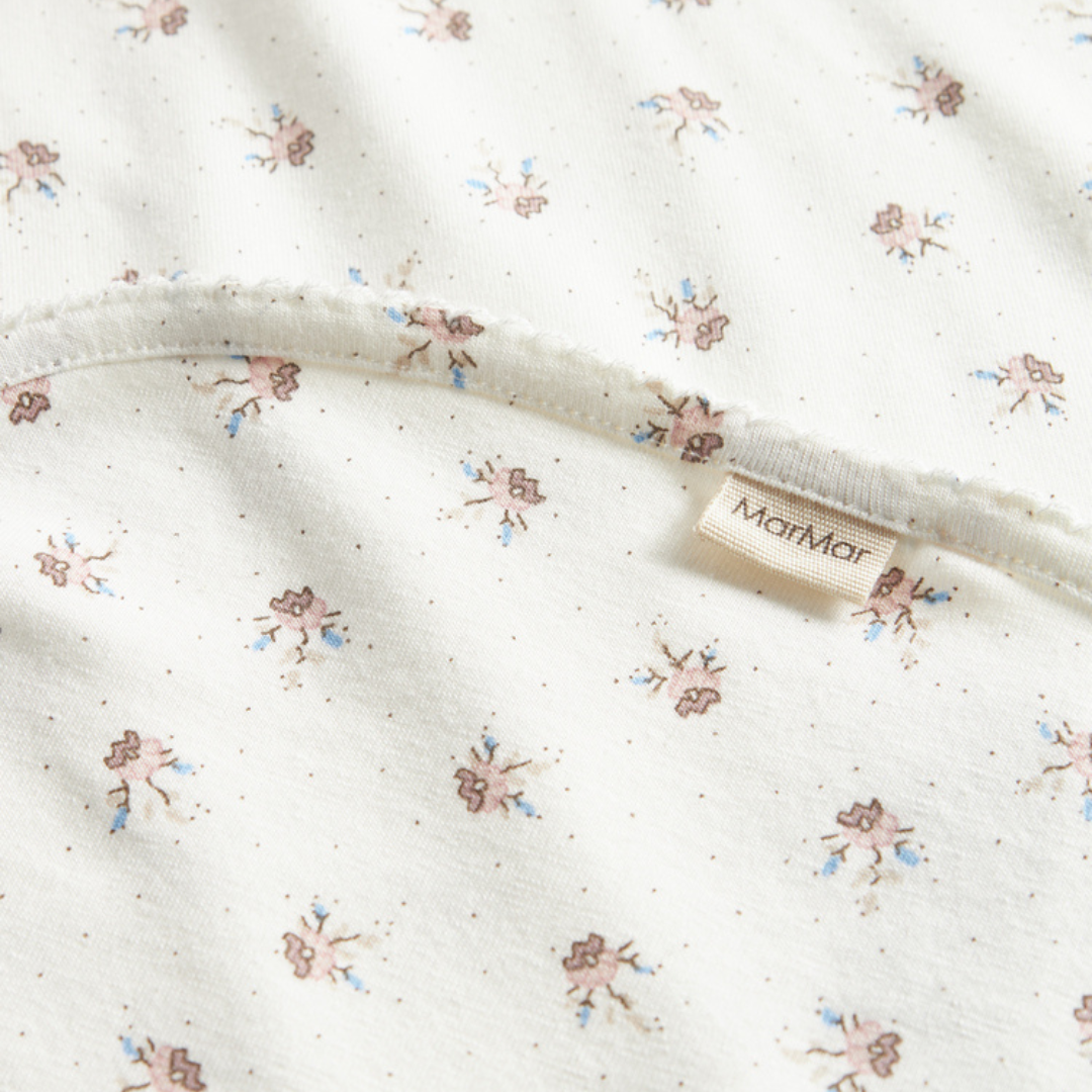 Sold at Bombon shop, designed by MarMar Copenhagen — white organic cotton baby blanket with floral print, part of a matching set.